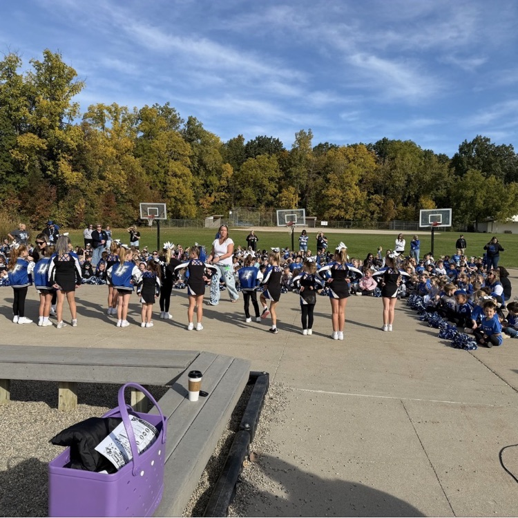 large group of students watching a pep assembly outside with a bright blue sky