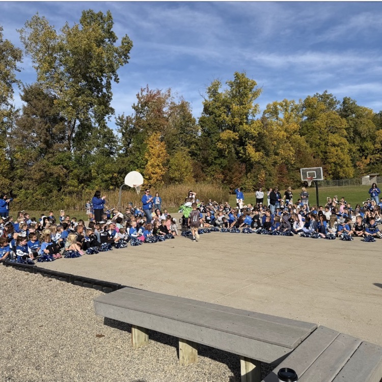 large group of students watching a pep assembly outside with a bright blue sky