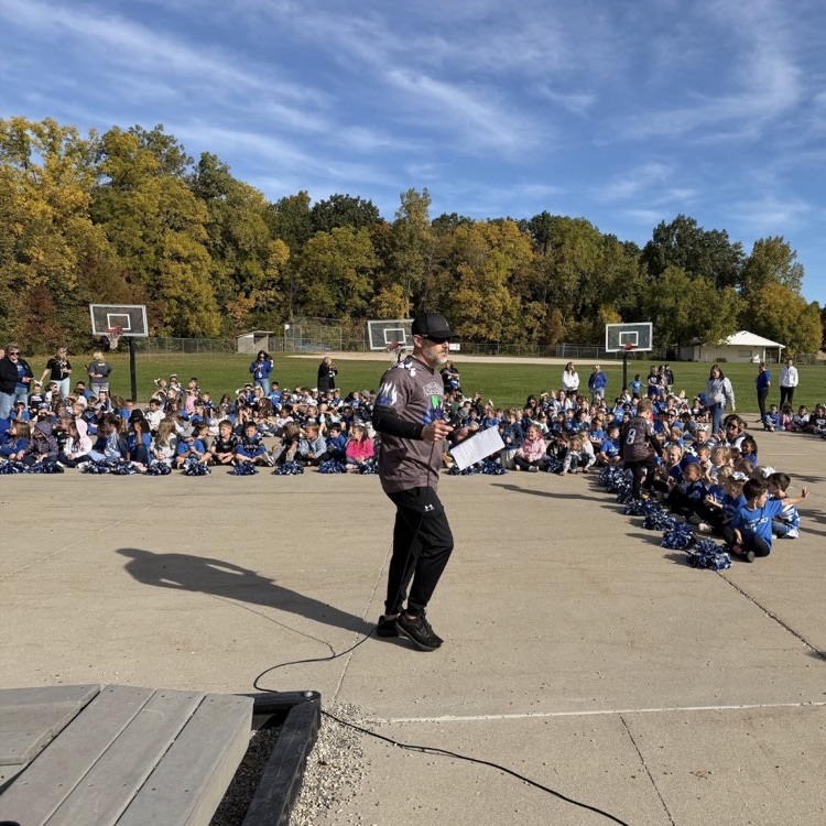 large group of students watching a pep assembly outside with a bright blue sky
