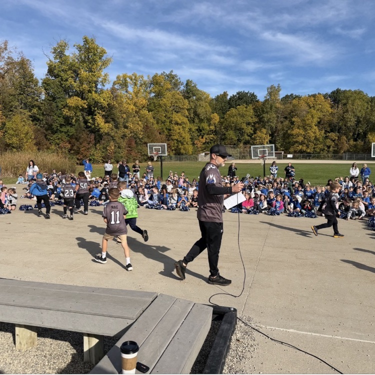 large group of students watching a pep assembly outside with a bright blue sky