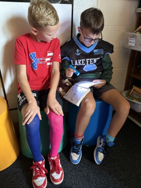 2 boys  reading in a classroom with flashlights and stuffed animals