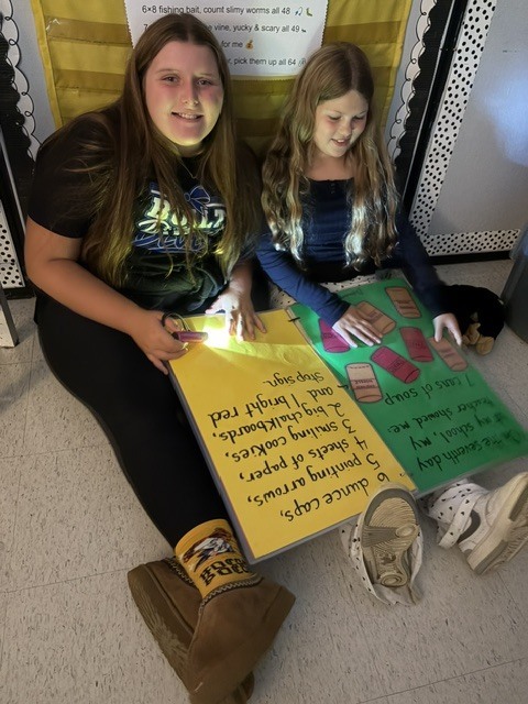 2 girls reading on a classroom floor with flashlights and stuffed animals