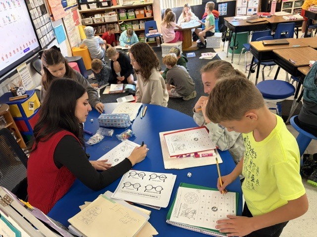group of students working at a desk with a teacher