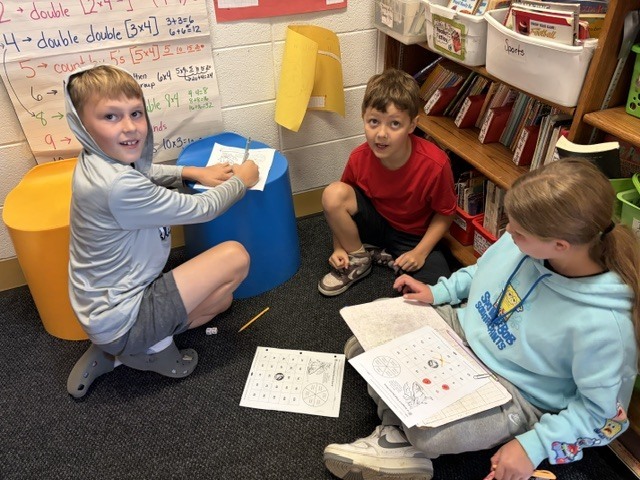 3 students doing homework on the floor in a classroom