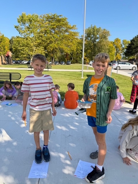 2 boys standing on a sidewalk and smiling