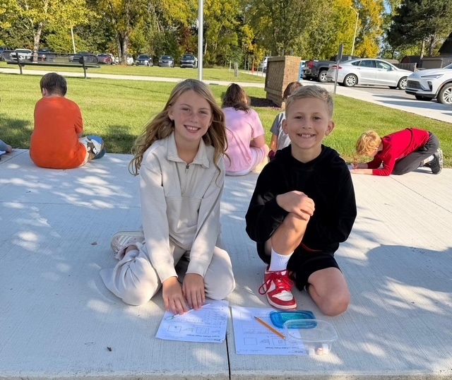 2 kids sitting outside doing schoolwork