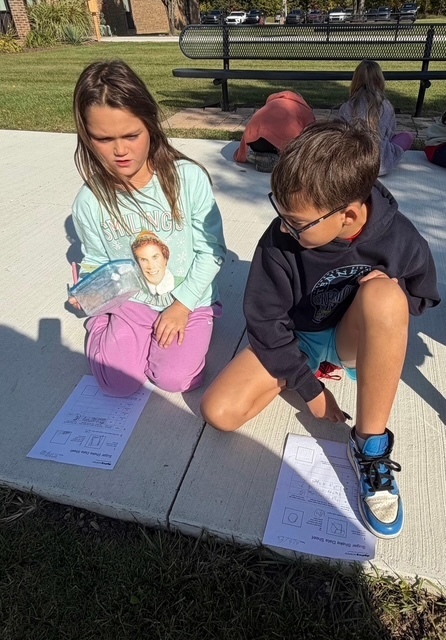 2 kids doing schoolwork on a sidewalk outside