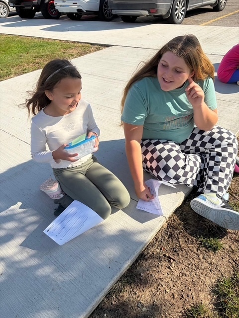 2 girls sitting outside doing schoolwork
