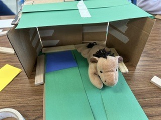 stuffed horse on a green piece of construction paper in a box house