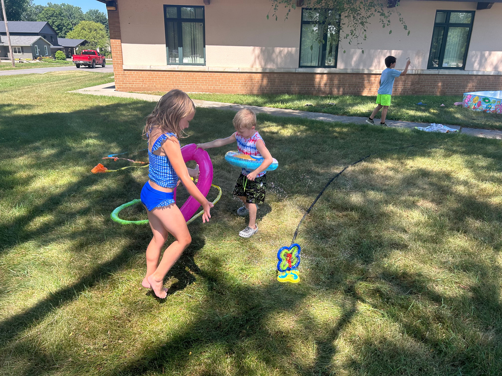 kids playing outside in grass with hose