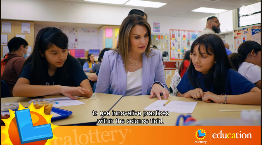 "Lamont Elementary School District Superintendent Lori González sits at a classroom table with two students, reviewing a science activity worksheet. The image includes California Lottery and education logos in the corner, highlighting support for innovative practices in education.
