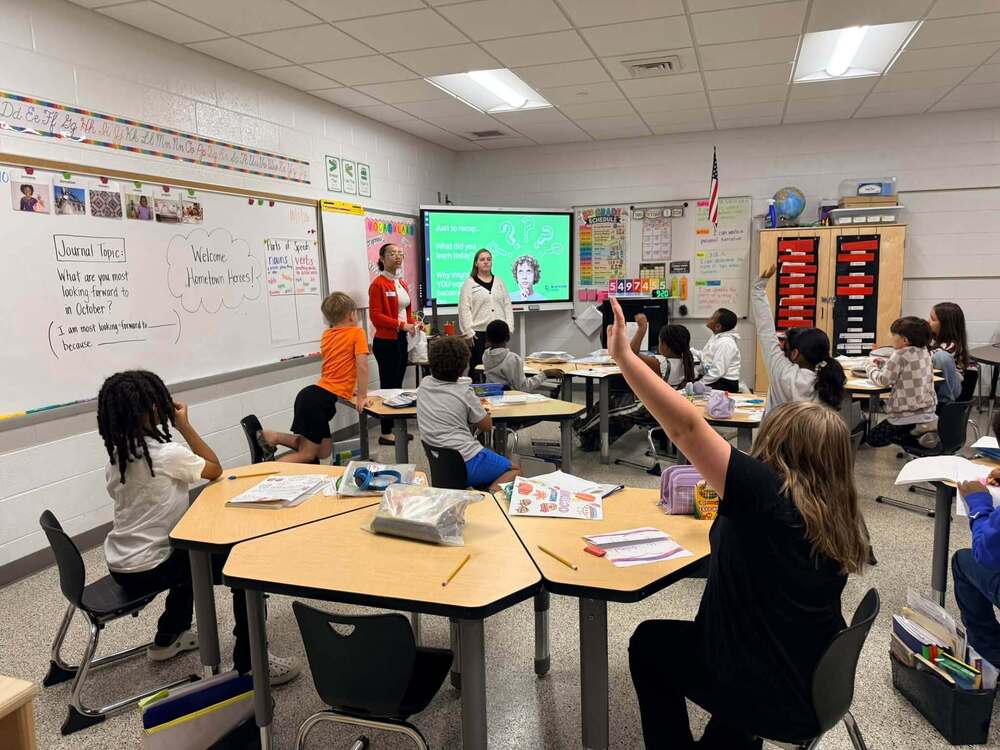 LES students in a 3rd grade classroom raising their hand getting ready to ask the Blue Rdige Bank workers a question