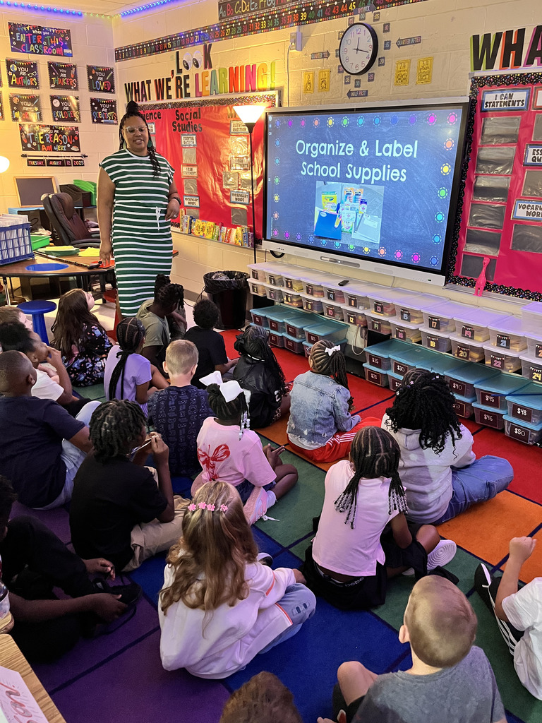 Students sitting on a rug listening to their teacher