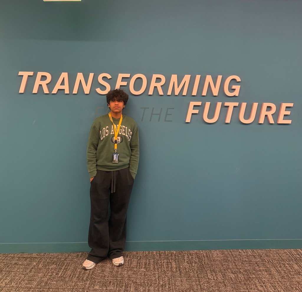 A boy stands in front of a teal wall that has the phrase: "TRANSFORMING THE FUTURE."