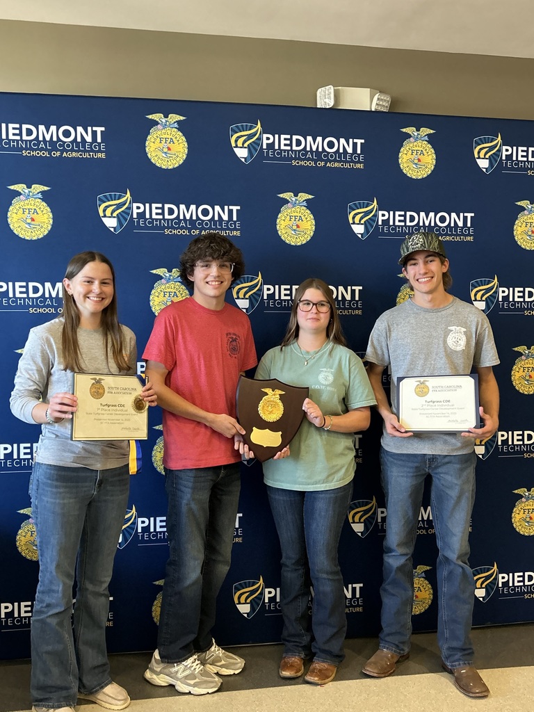 Four smiling students (two girls, two boys) posed before a blue backdrop with multiple logos reading "PIEDMONT TECHNICAL COLLEGE SCHOOL OF AGRICULTURE" and FFA circular emblems. Two students hold certificates and one holds a shield-shaped award. No other readable text on clothing or certificates.