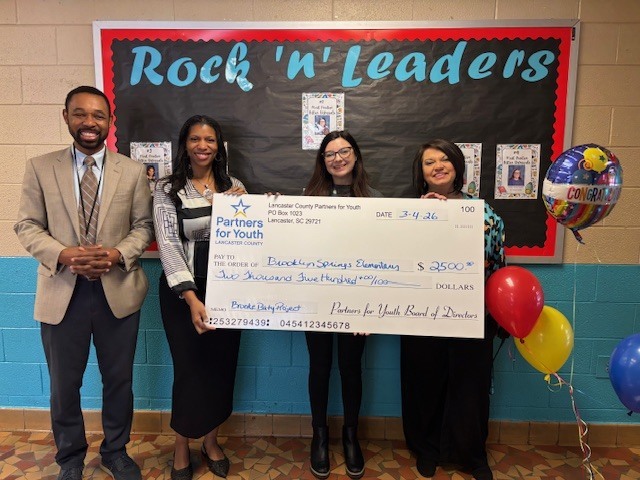 Mr. Blair, Miss King, Miss Baty, and Mrs. McManus with a large check and balloons