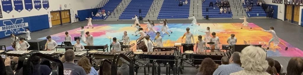 color guard preforms on a multicolored floor in white costumes