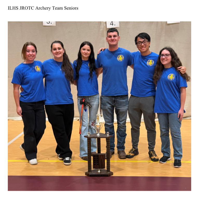 Six ILHS JROTC Archery Team seniors—three females and three males—stand side-by-side on a gymnasium floor wearing matching blue t-shirts with yellow circular logos. A multi-tiered silver trophy sits on a stand in front of the group. Numbers '3' and '4' are visible on the wall behind them."