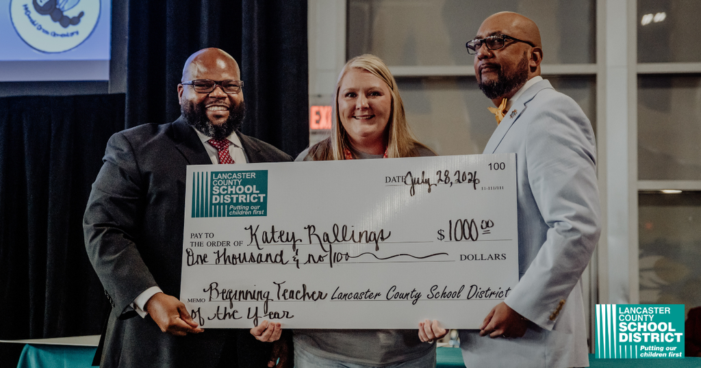 Three people hold a check, with one person presenting it to a woman in the center.