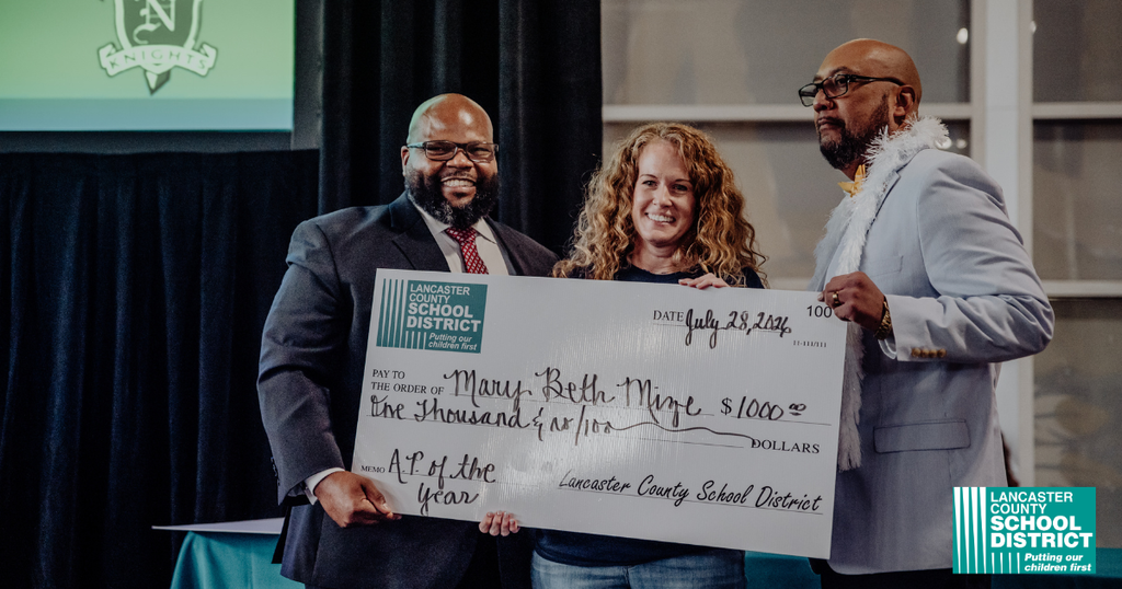 Three people hold a large check, standing close together. One holds the check while the others flank them.