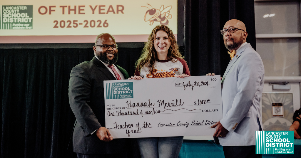 Three people stand with a large check. A woman in the middle holds the check. Two men stand on either side of her.