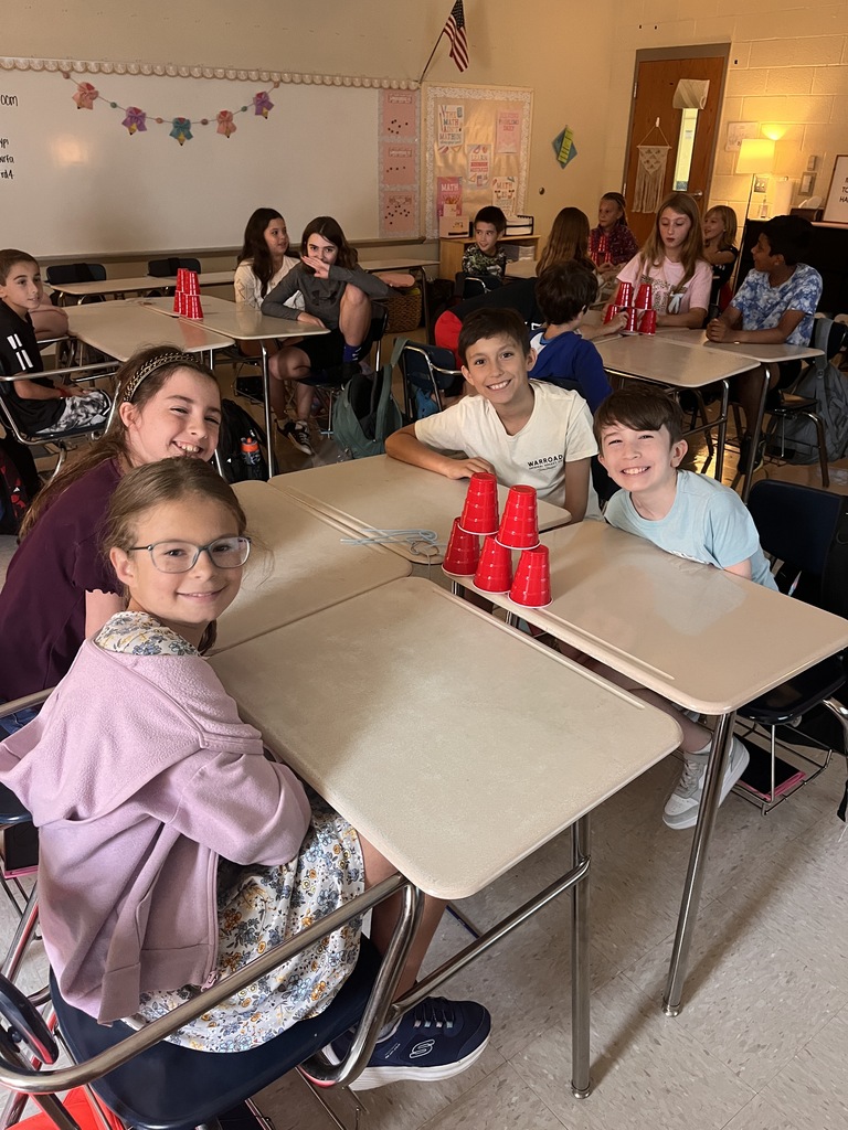 Classroom with students seated at desks. Three students in front with red cups in front.