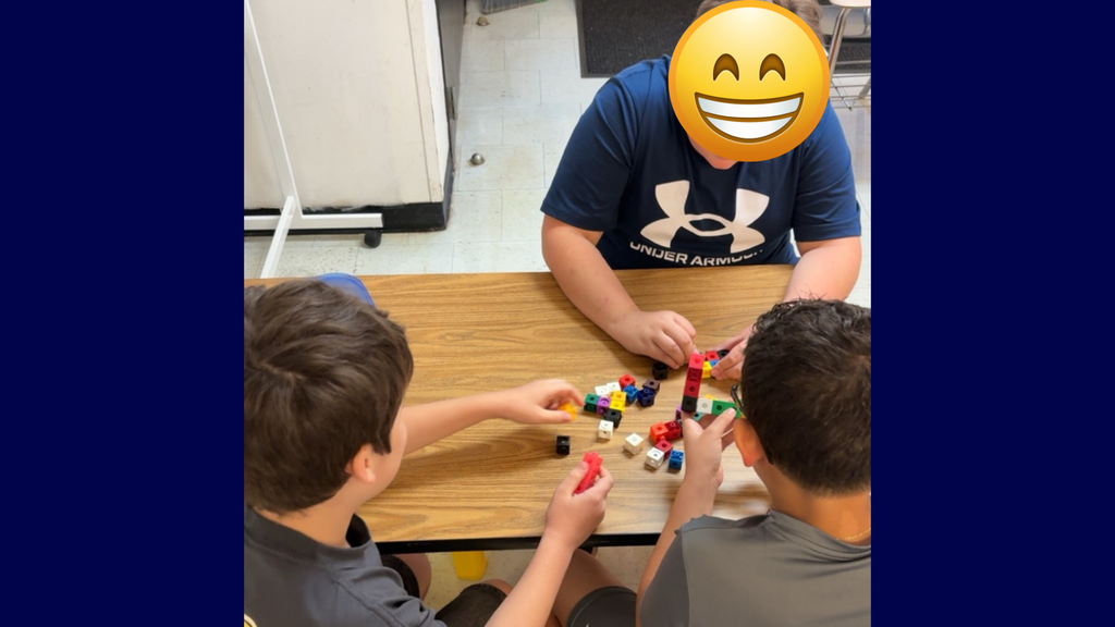 Three boys seated at a table, engaging with colorful cubes. One wears a blue shirt, another gray.