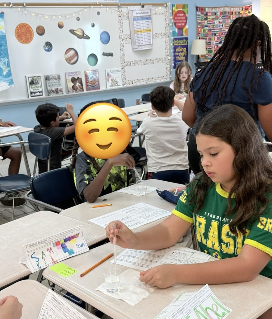 Students in a classroom are engaged in an experiment. A girl is holding a test tube with a liquid.