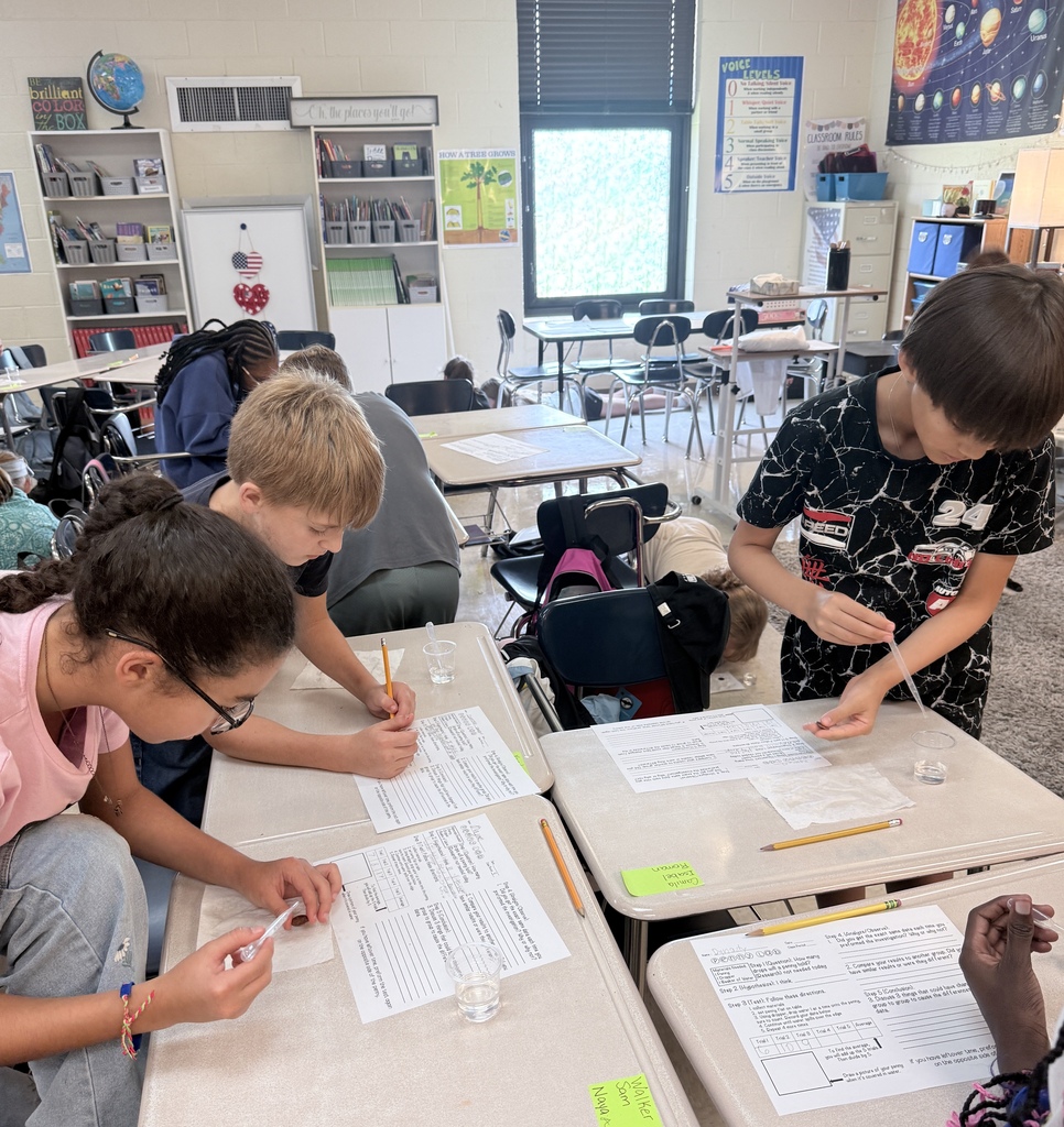 Four children are seated at desks in a classroom, engaged in an experiment with small containers.
