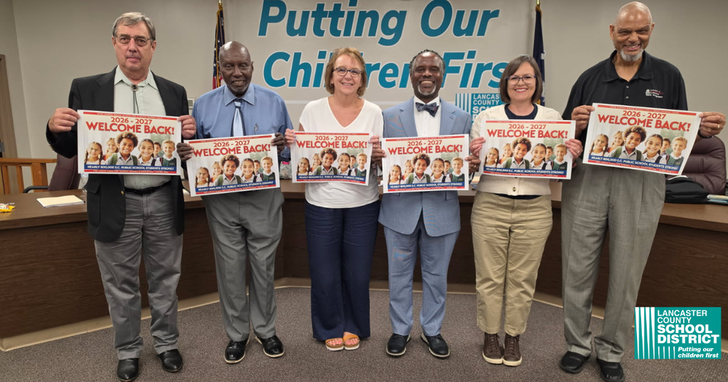 Six adults holding signs with "Putting Our Children First" and images of children. The background is a room with flags and a desk.