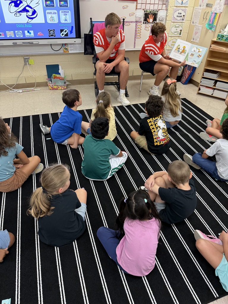 A teacher reading a book to a group of children in a classroom. Children sit on the floor.