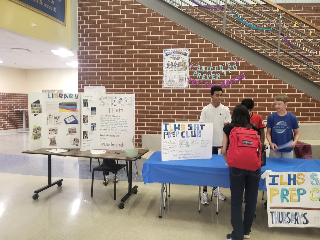 Students standing around tables with posters, one reading "IH Sit Prep Club" and another "ILHS Prep Club".