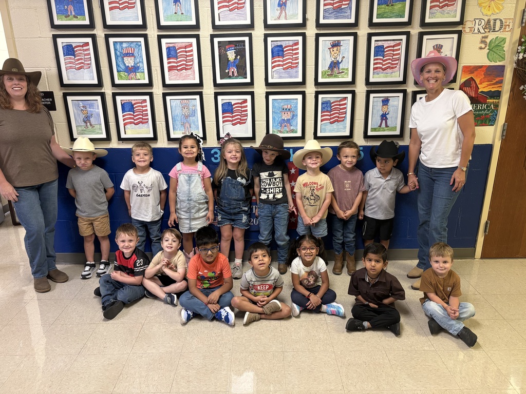 A group of young children in cowboy hats pose for a photo with two women in a classroom.