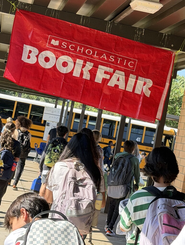 image of students getting to the buses with a scholastic book fair banner 