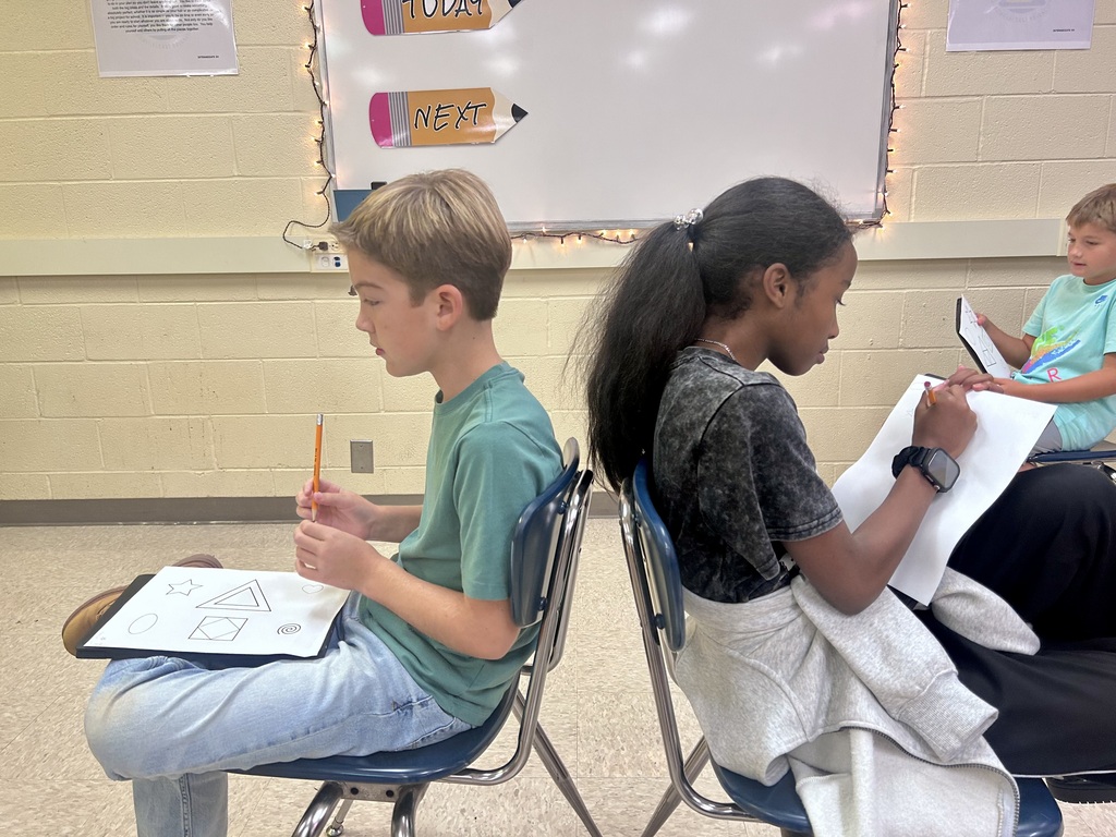 Three students work on papers in a classroom. One boy and two girls. A whiteboard in the background has "Today" and "Next" written on it.