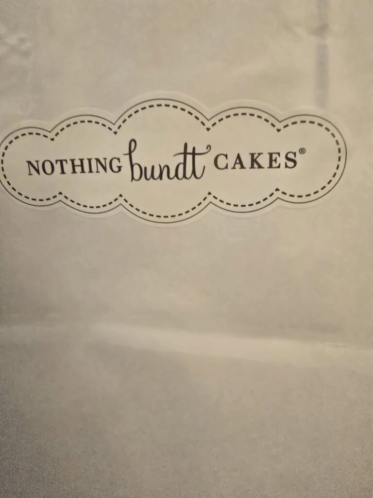 A white paper bag with a logo that reads "Nothing Bundt Cakes" in black lettering.