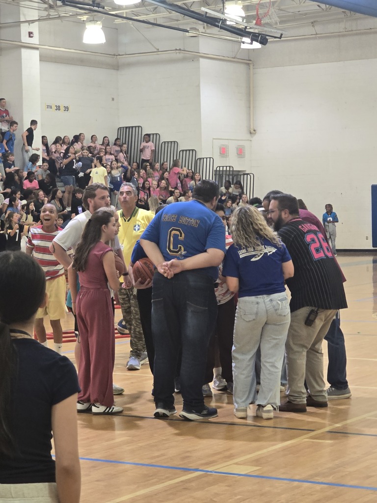 A group of people in a gymnasium with bleachers, all facing towards a central point on the court.