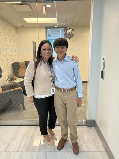 A woman and boy stand in a room with white flooring and glass walls, smiling and posing for a photo.