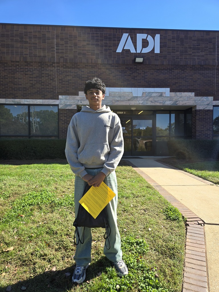 A person in a gray sweatshirt holds a yellow folder and stands in front of a brick building.