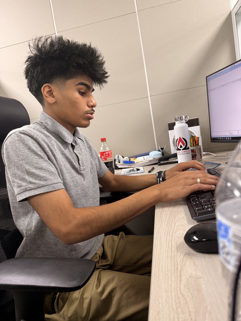 A person sits at a desk with a computer, typing on the keyboard. A water bottle is on the desk.