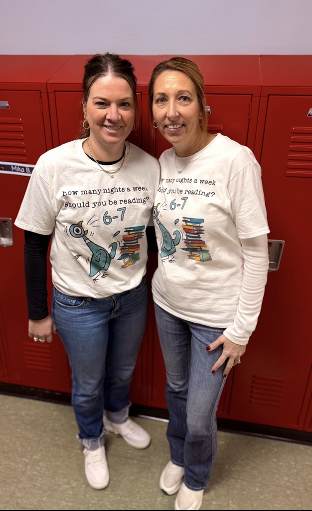 Two individuals standing in front of red lockers wearing matching white shirts featuring a cartoon pigeon and a stack of books. The shirts read: “How many nights a week should you be reading? 6-7.” Both are wearing jeans and casual shoes.