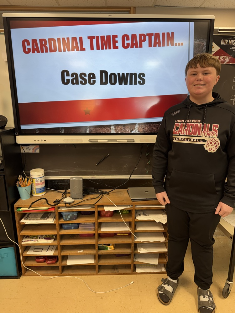 a sixth grade boy standing in front of a smart board that reads Cardinal time captain 