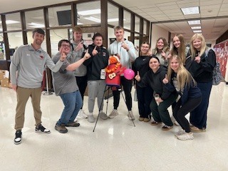 Mr. Groth's group- A group of students standing together in a school hallway with offices behind them, wearing casual clothing and backpacks.