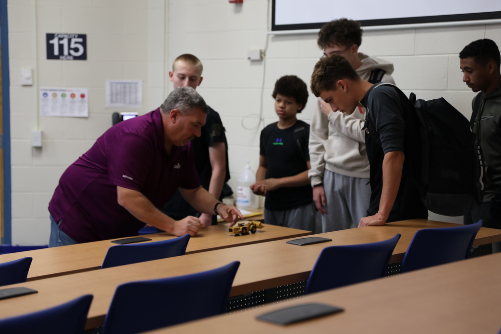 five students looking as an expert from Cargill demonstrations the machinery used in the mine with a toy model