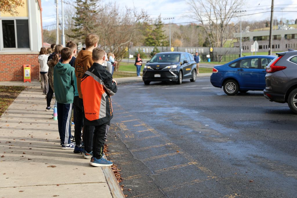 Middle school students cheer and wave as the student athletes drive by 