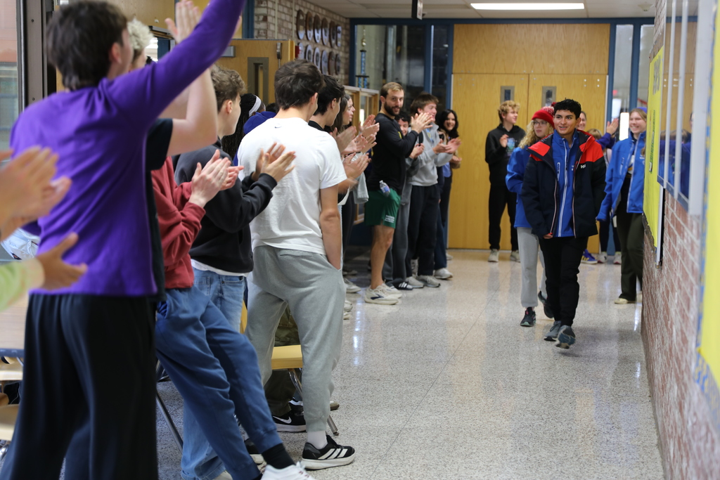 3 students walk down a hall as they are cheered on by many classmates