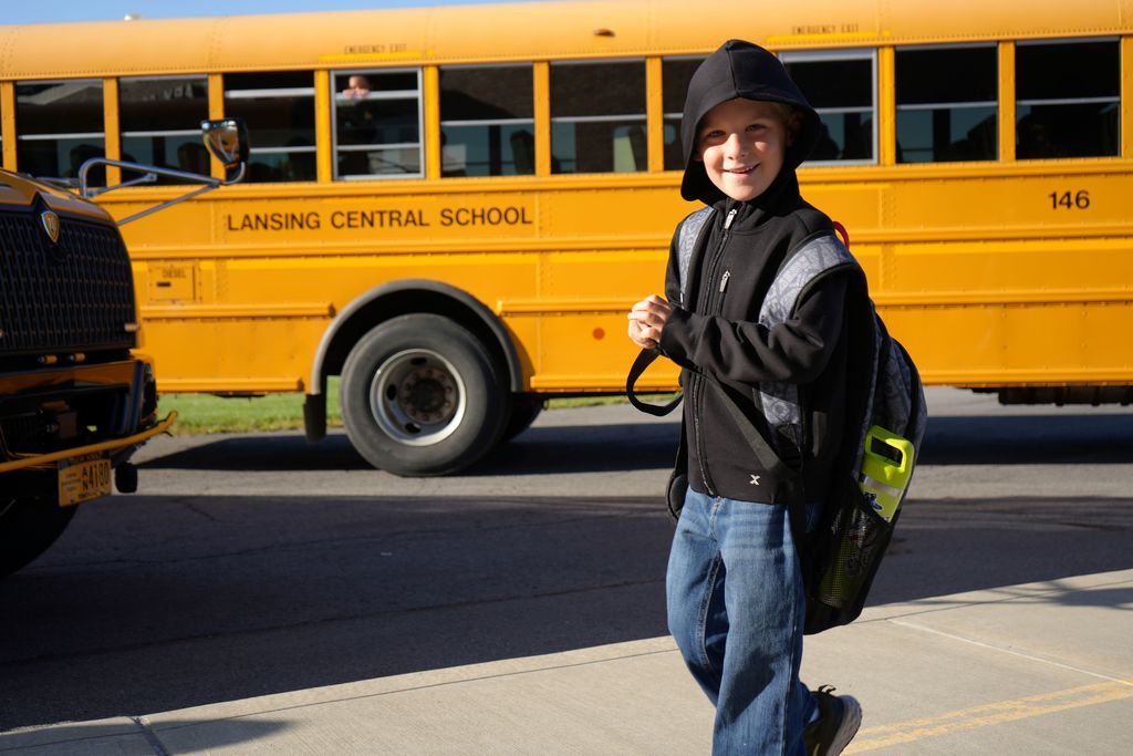student smiling walking by bus before entering school