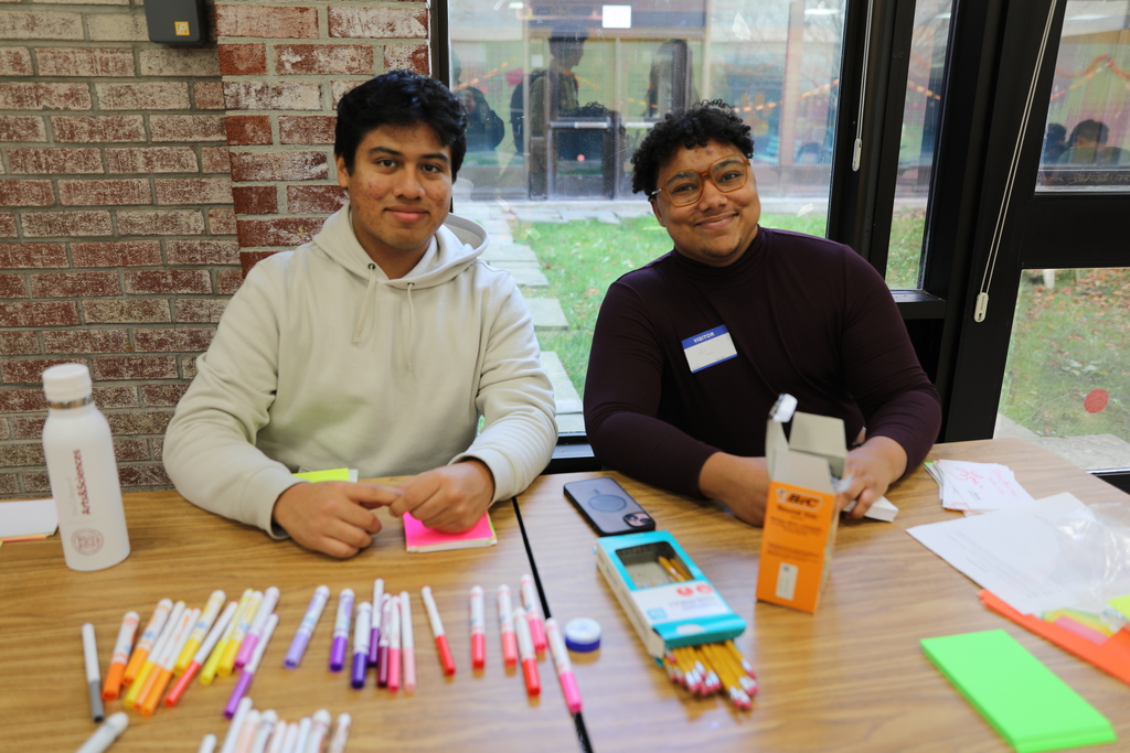 two students sitting at the reception desk for the event, handing out pens and note cards