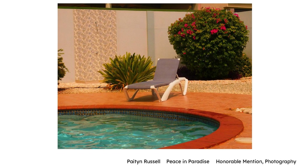 Paityn Russell – “Peace in Paradise” (Photography) Alt text: A quiet poolside scene with a curved swimming pool in the foreground and an empty lounge chair on a tiled patio. Tropical plants and flowering bushes surround the area, creating a calm, sunlit atmosphere.