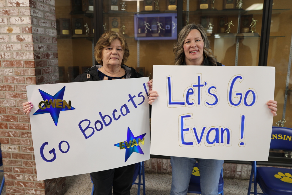 Parents of the wrestling students hold up their signs which read "Go Bobcats" and "Lets go Evan"